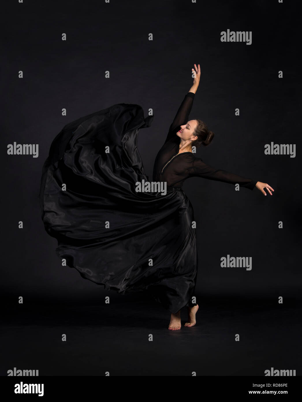A Young, smiling woman in black suit dancing modern choreography.Studio shot on dark background, isolated image. Stock Photo