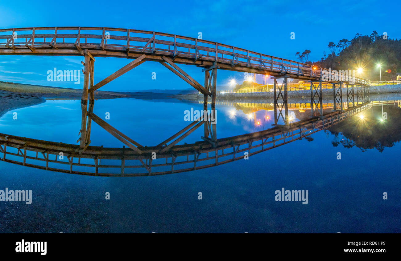 Old bridge illuminated with twilight colorful blue light on an awe natural scenery with a wooden bridge crossing the river and an illuminated promenade Stock Photo