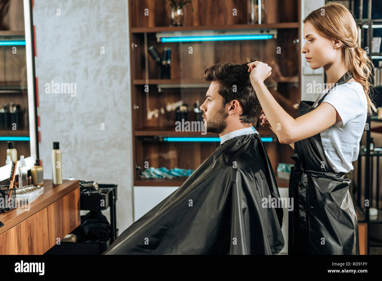 Side View Of Hairstylist Cutting Hair To Handsome Young Man In