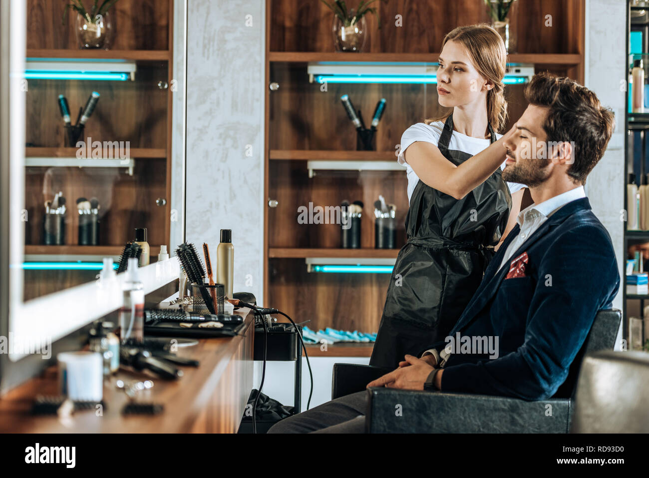 beautiful young hairdresser doing hairstyle to handsome client and