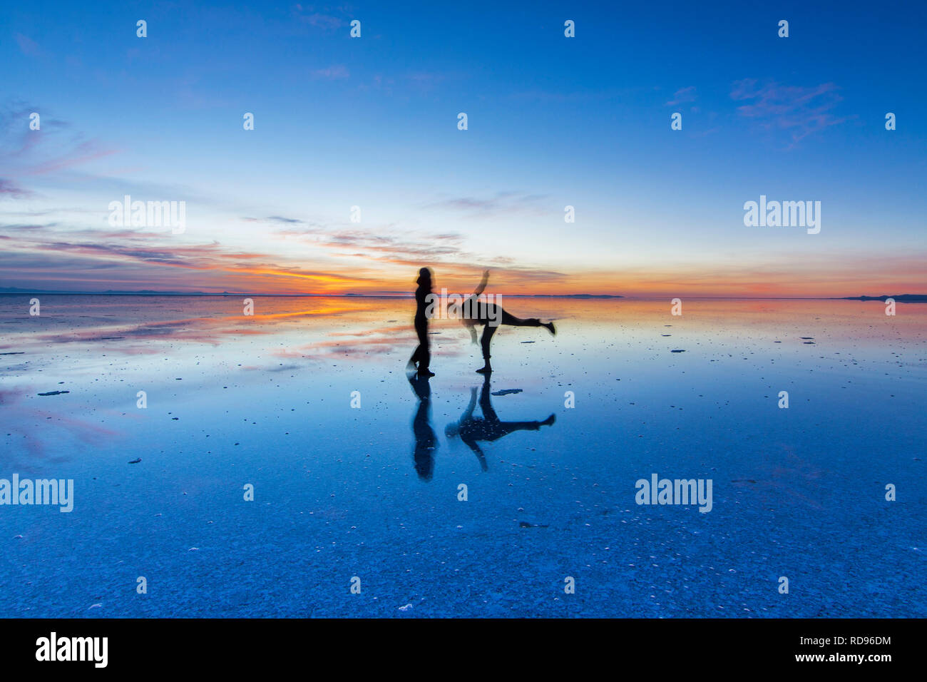 Couple looking to Sunrise at Uyuni saltflats. Sunrise over an infinite horizon in Salar de Uyuni with people reflections in water, a colorful scenery Stock Photo