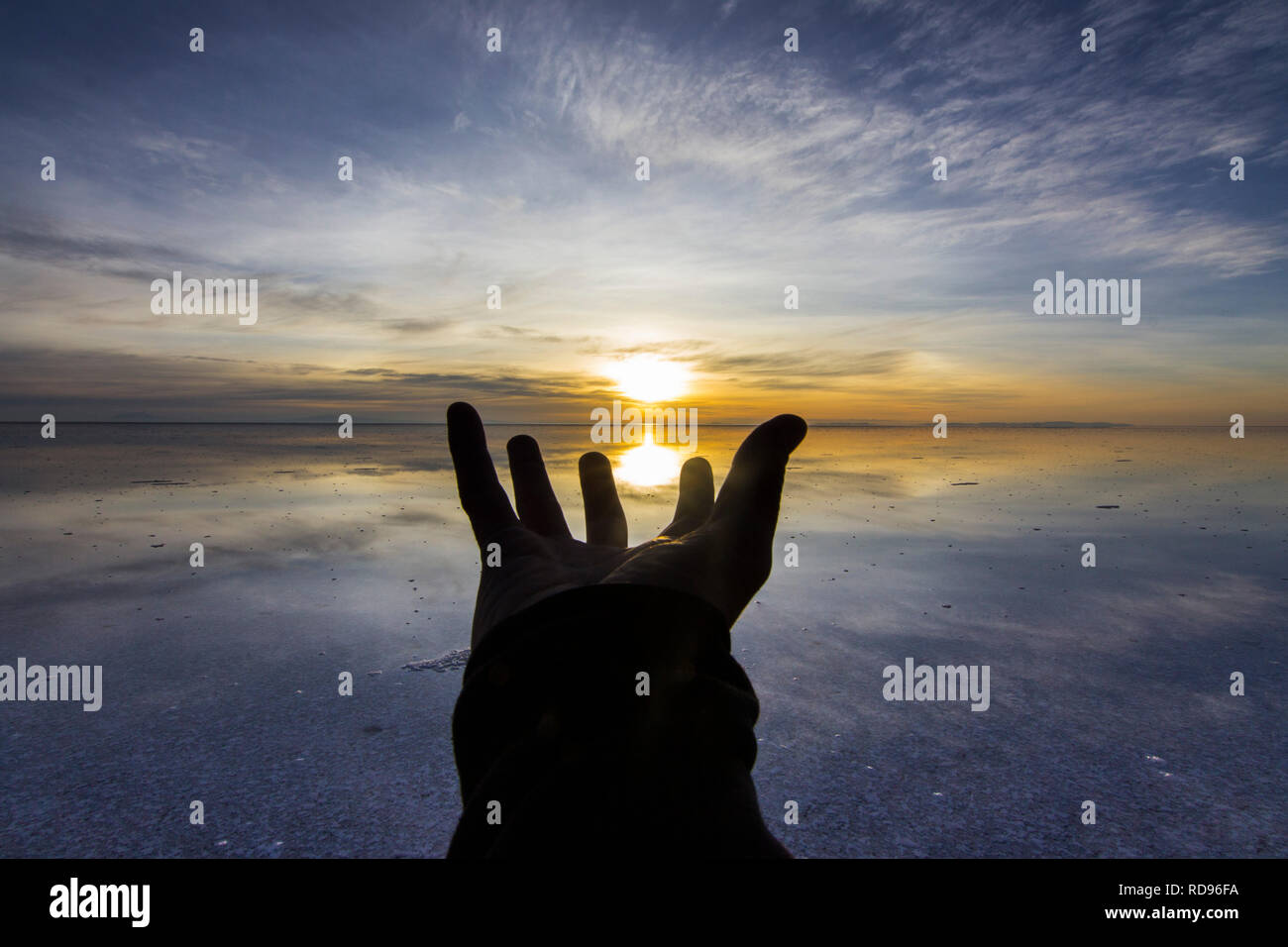 A hand for hope on this amazing Planet Earth.  Trying to catch the sun at Uyuni saltflats inside an idyllic colorful scenery with reflections in water Stock Photo