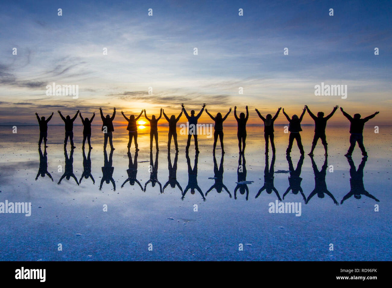 Amazing real people reflections in water at Uyuni Saltflats scenery. People playing with the reflections over the salt lake during a colorful sunrise Stock Photo