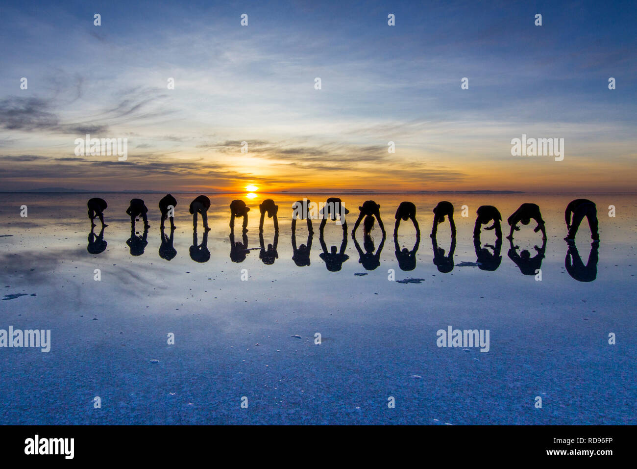 Amazing real people reflections in water at Uyuni Saltflats scenery. People playing with the reflections over the salt lake during a colorful sunrise Stock Photo