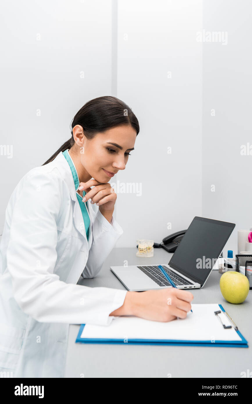 pensive female doctor making notes near laptop Stock Photo - Alamy