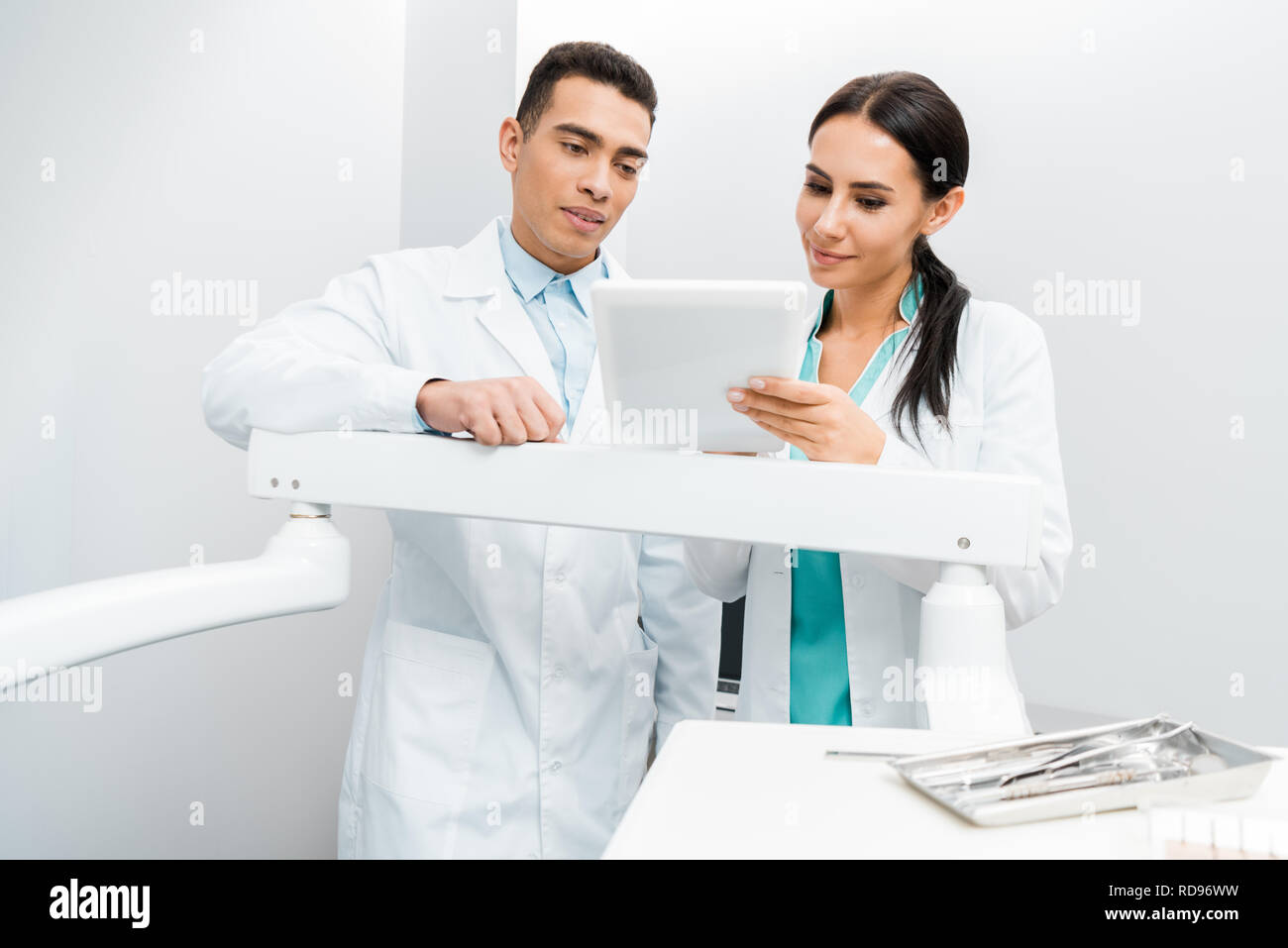 multicultural doctors standing in white coats and looking at digital ...