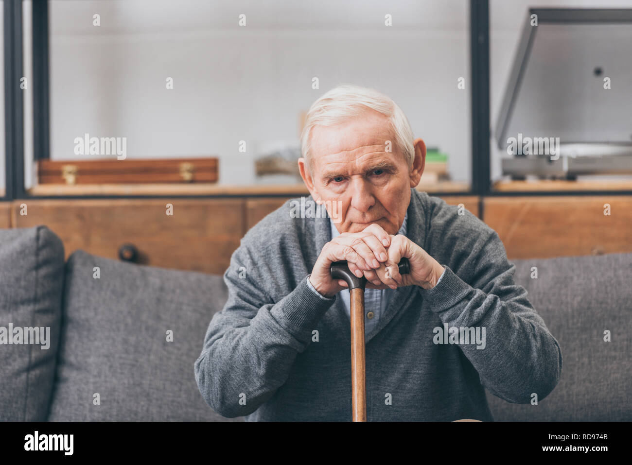 upset retired man with grey hair sitting with walking cane in living room Stock Photo