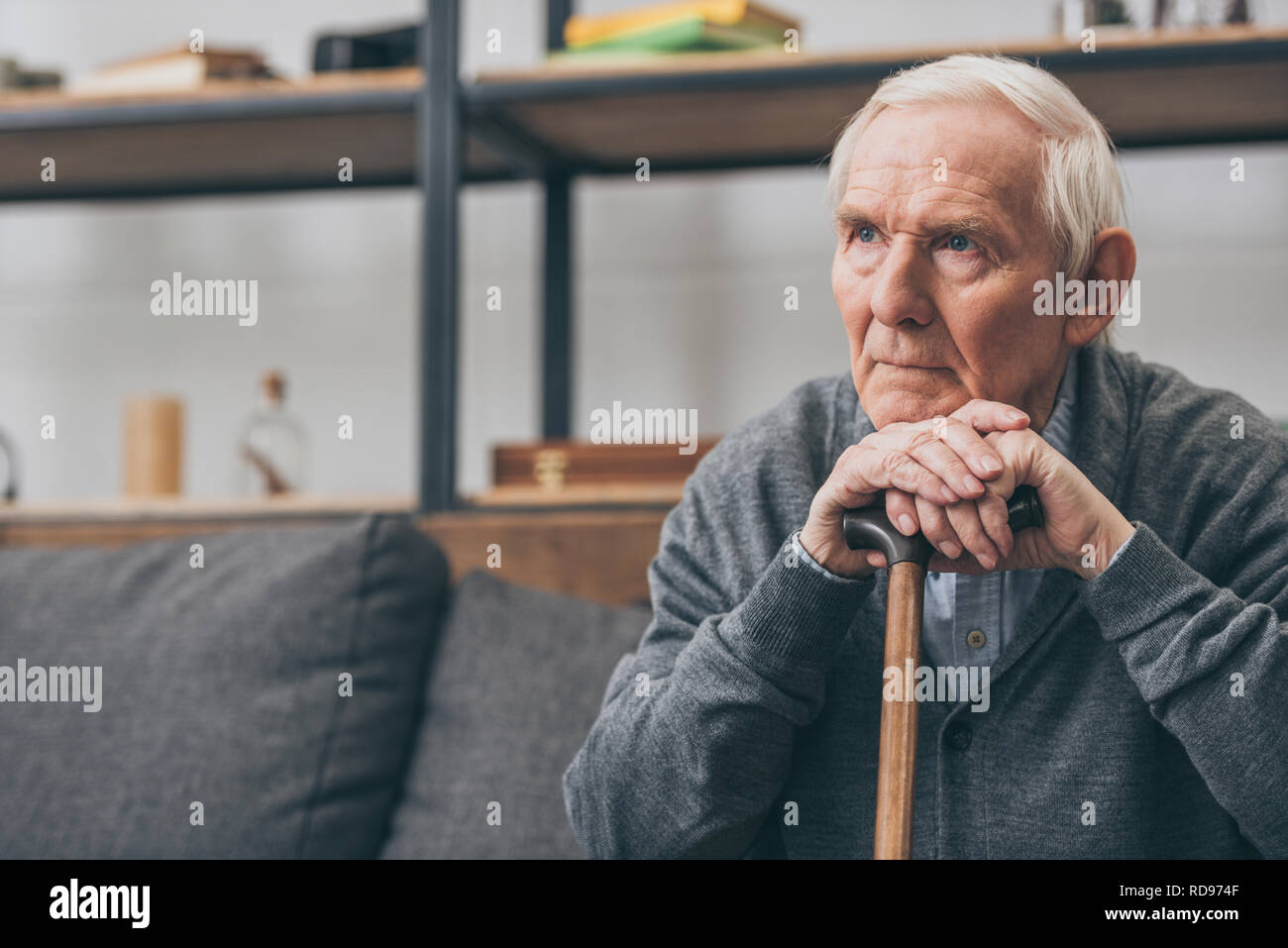 sad retired man with grey hair holding walking cane in living room Stock Photo