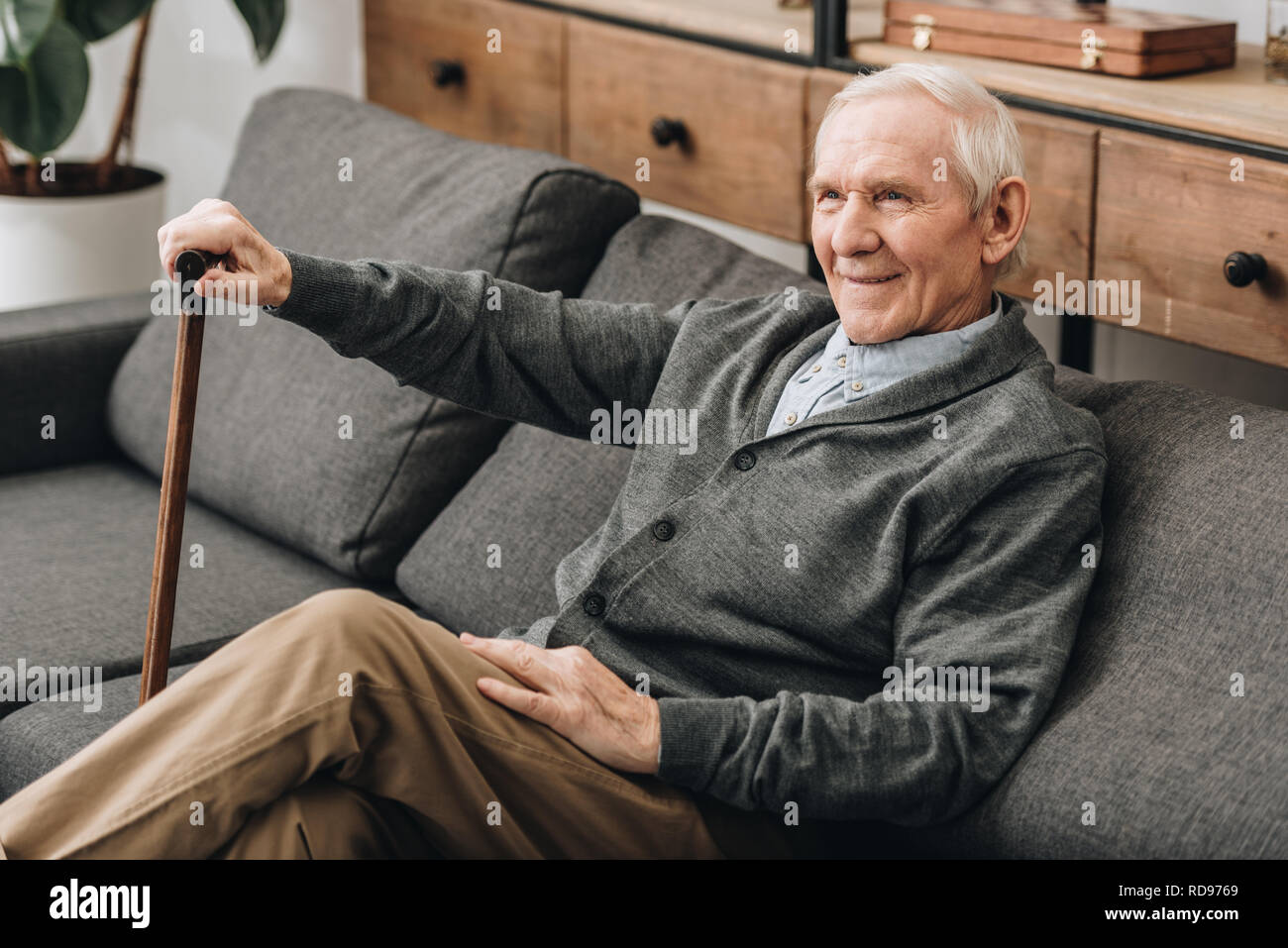smiling retired man sitting on sofa with walking cane Stock Photo - Alamy