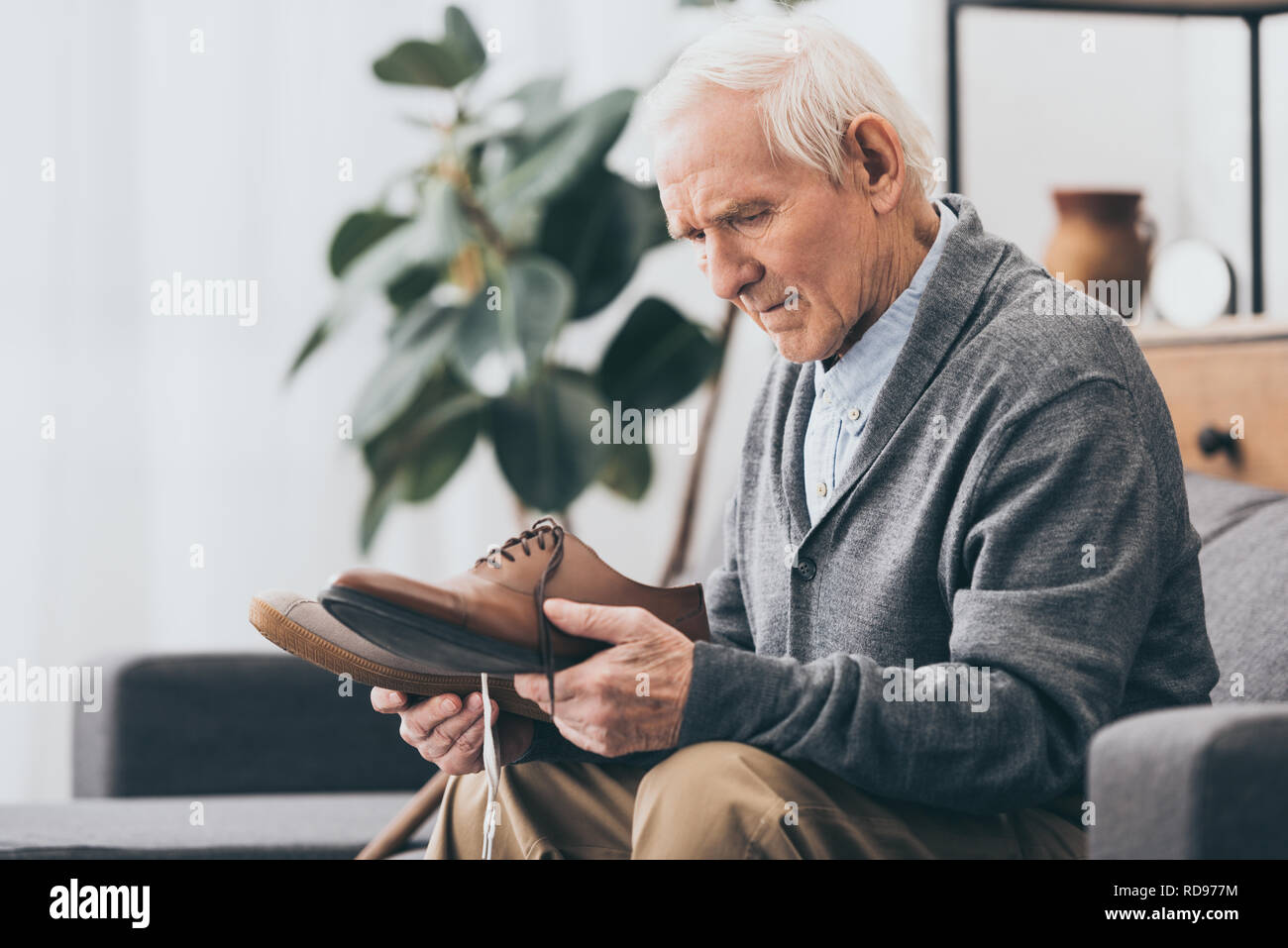 senior man holding shoes in hands while sitting on sofa Stock Photo
