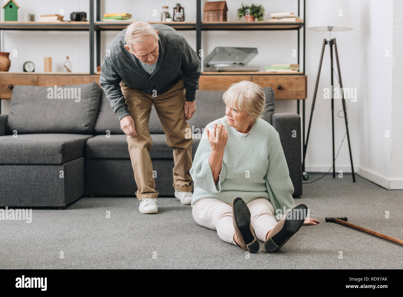 retired husband coming to upset senior wife sitting on floor with walking cane Stock Photo