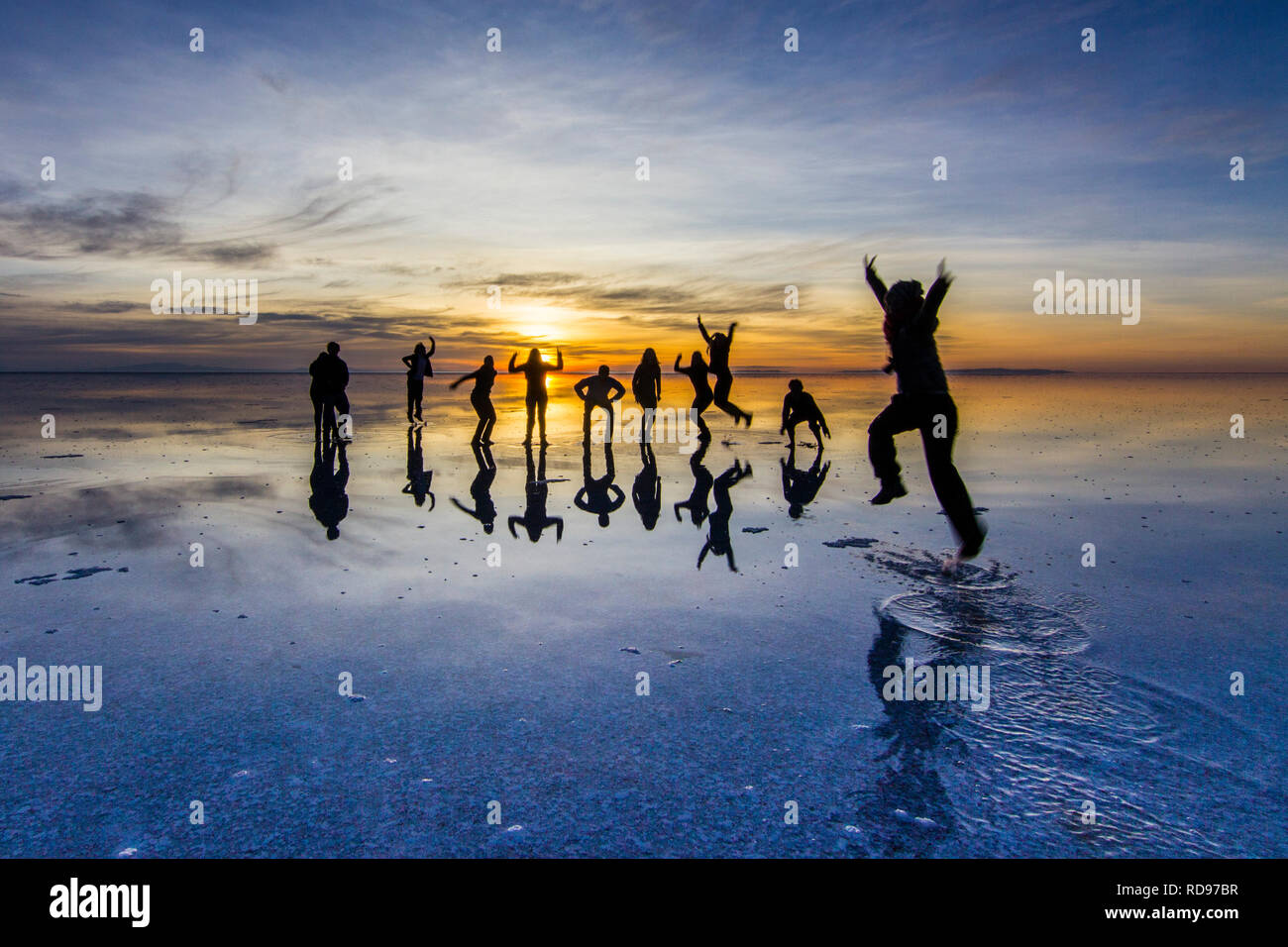 Amazing real people reflections in water at Uyuni Saltflats scenery. People playing with the reflections over the salt lake during a colorful sunrise Stock Photo