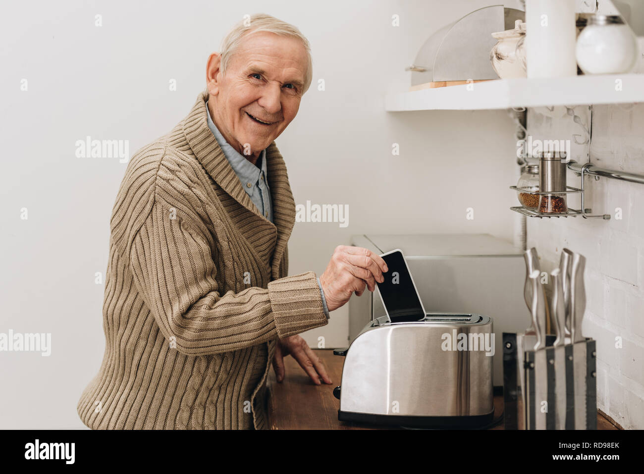 happy senior man with dementia disease putting smartphone in toaster