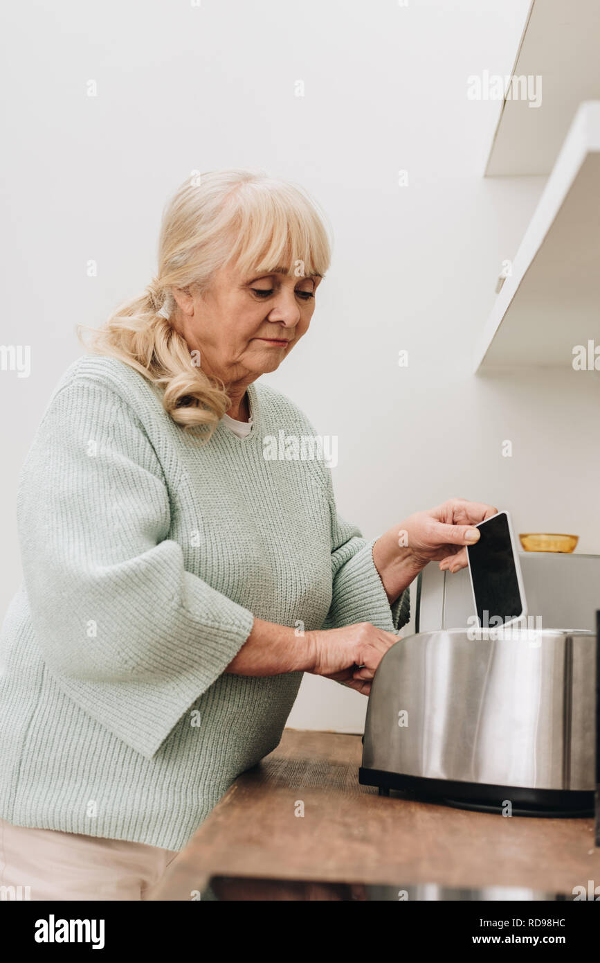 retired woman with dementia disease putting smartphone in toaster Stock