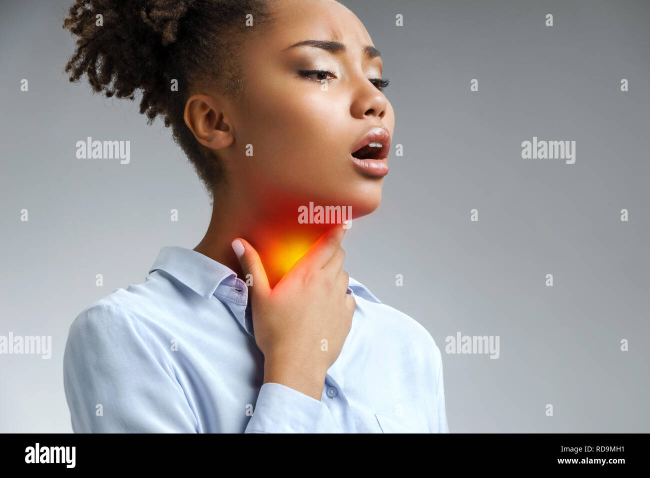 Throat pain. Woman holding her inflamed throat. Photo of african american woman in blue shirt on gray background. Medical concept Stock Photo
