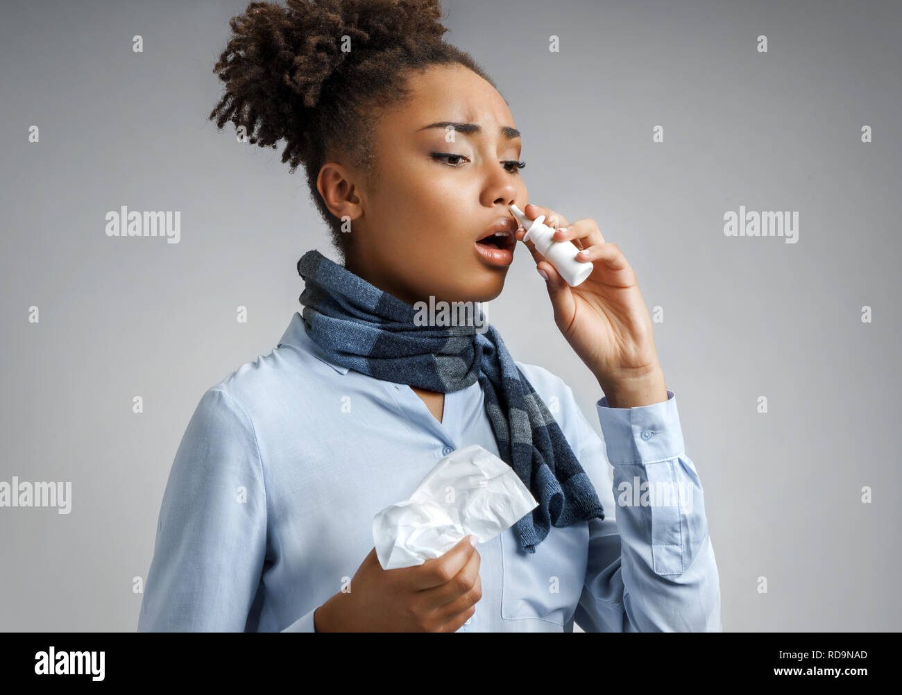 Woman using nose spray. Photo of african american woman in blue shirt on gray background. Medical concept Stock Photo