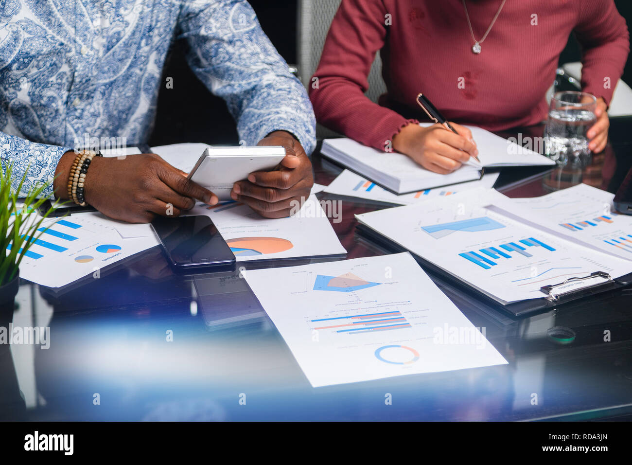 hands of dark-skinned people hold calculator against background of financial documents in business space closeup Stock Photo