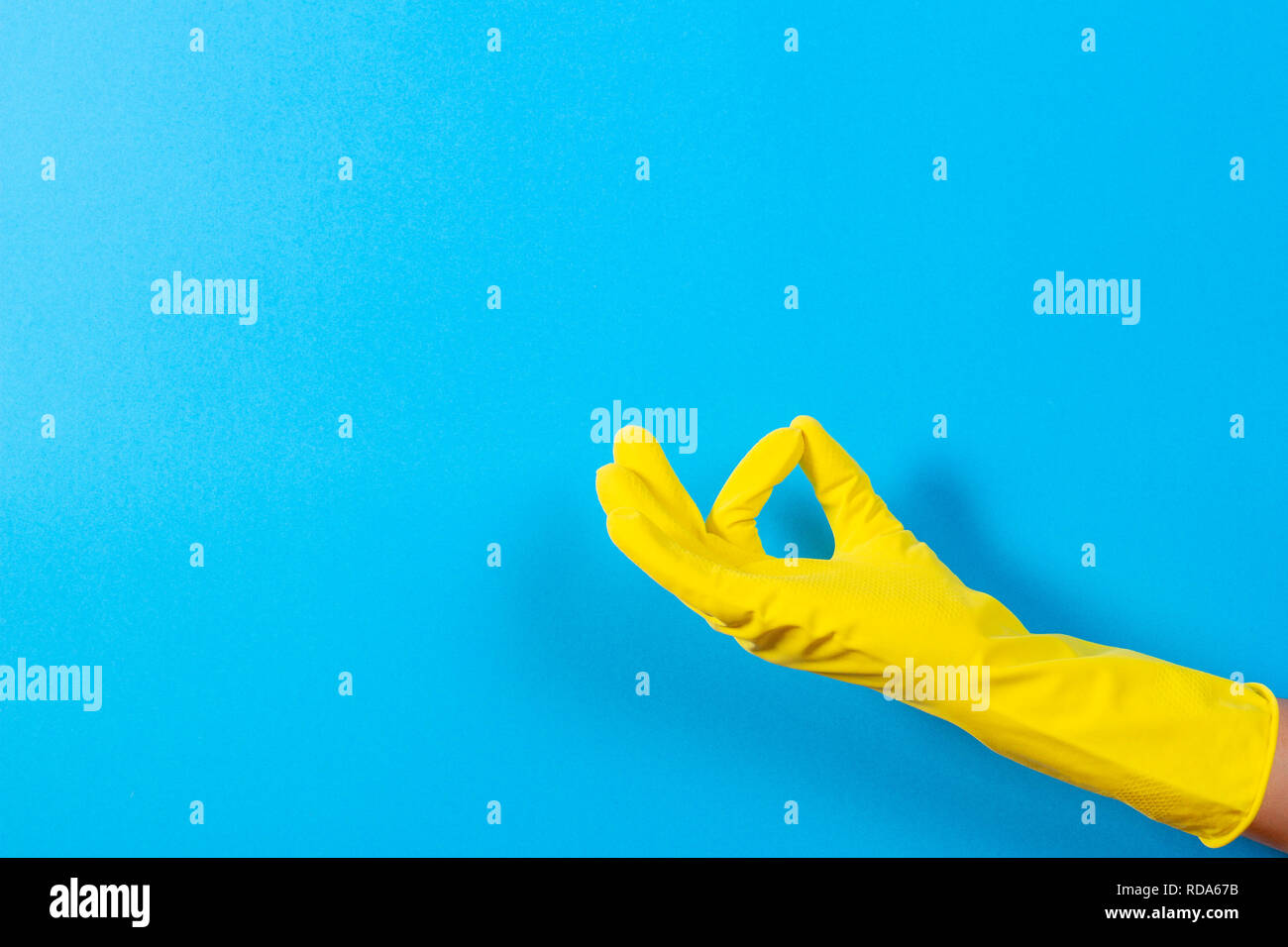 Woman hand with yellow rubber glove making a gesture meaning ok, top view on blue background Stock Photo