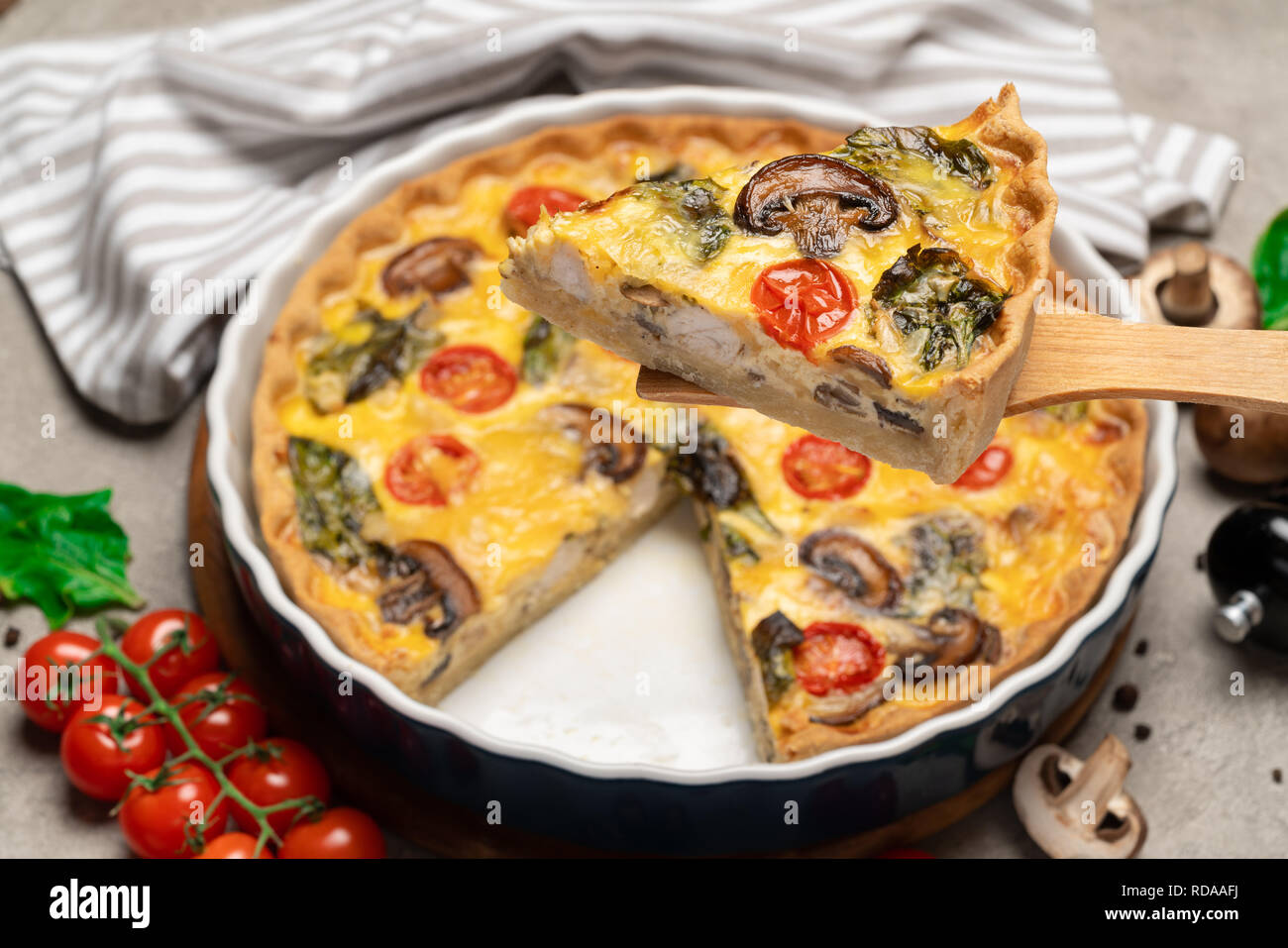 Baked homemade quiche pie in ceramic baking form and slice on wooden paddle Stock Photo