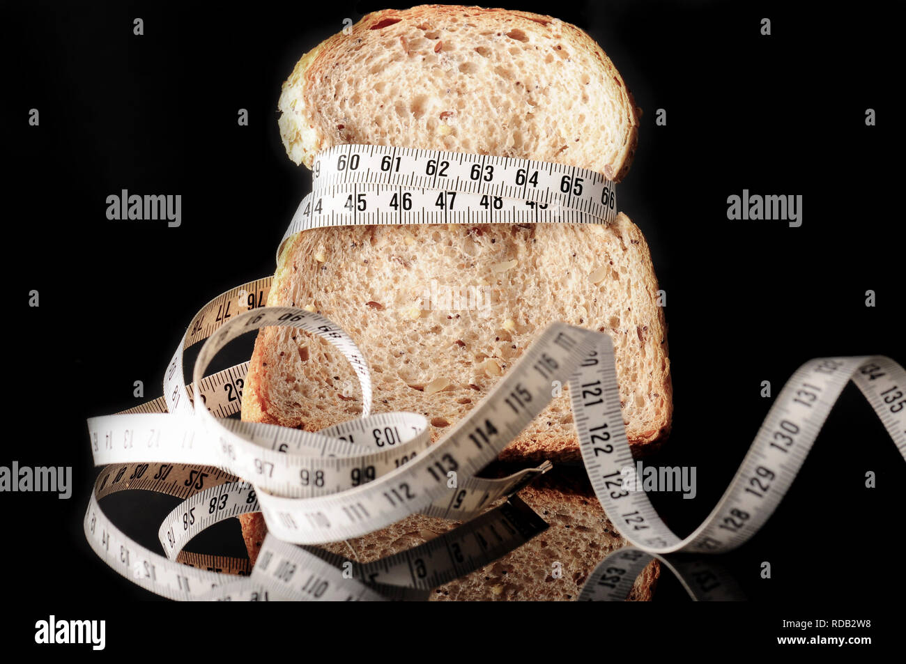 A slice of bread surrounded by a measurement tape on black with reflection Stock Photo
