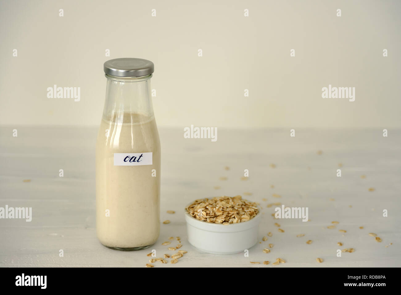 Glass bottle of oat milk on white background. Bowl with oatmeal flakes near it Stock Photo