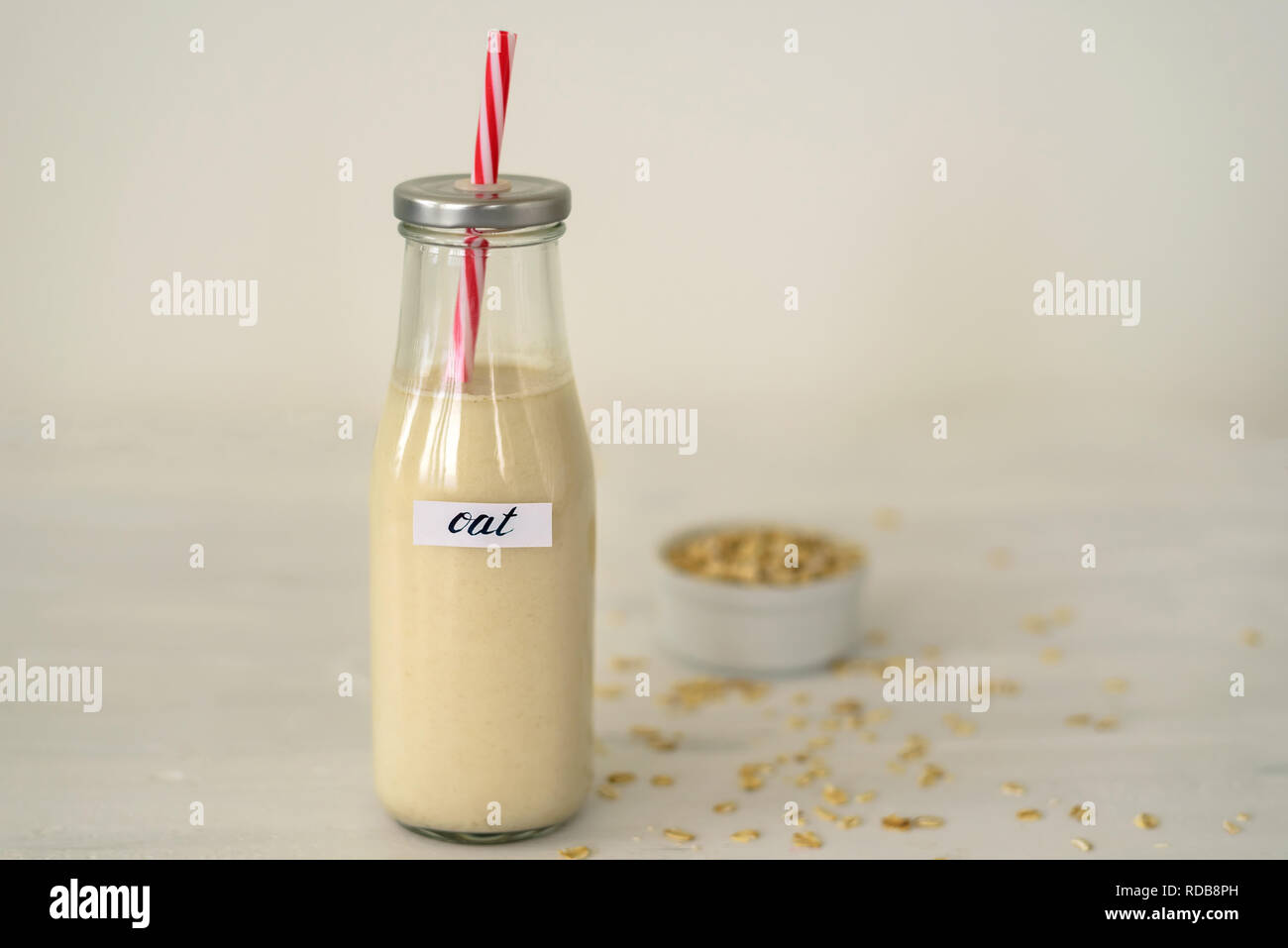 Glass bottle of oat milk on white background. Bowl with oatmeal flakes near it Stock Photo
