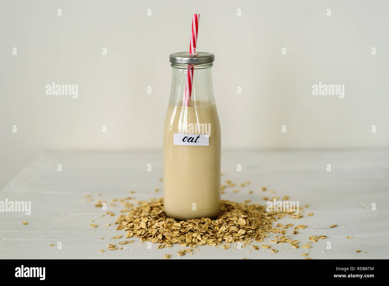 Glass bottle of oat milk on white background behing heap of oatmeal flakes Stock Photo