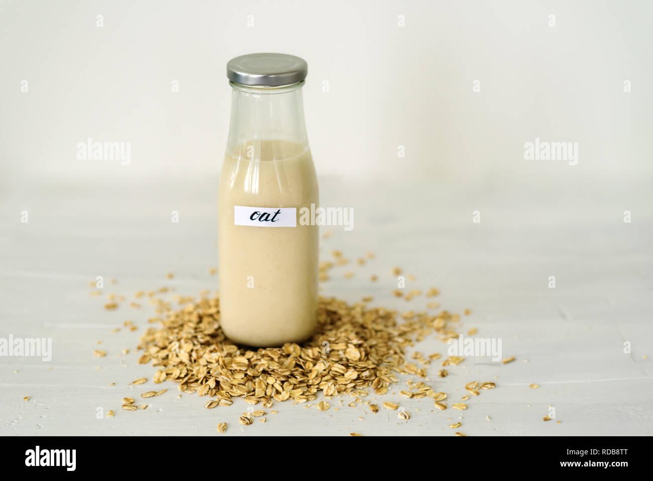Glass bottle of oat milk on white background behing heap of oatmeal flakes Stock Photo