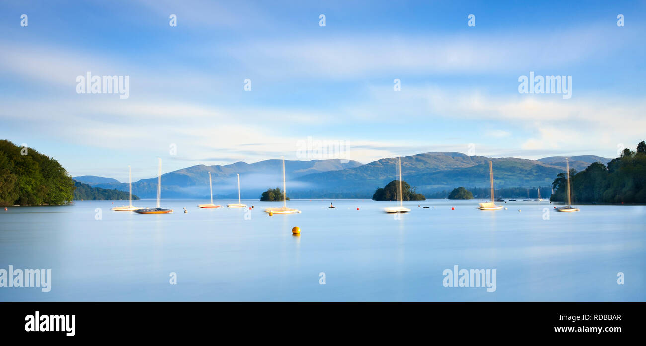 Bright cool blue sunrise looking up Lake Windermere through the boats towards Ambleside. Long exposure adds motion & reflection to boats and clouds Stock Photo