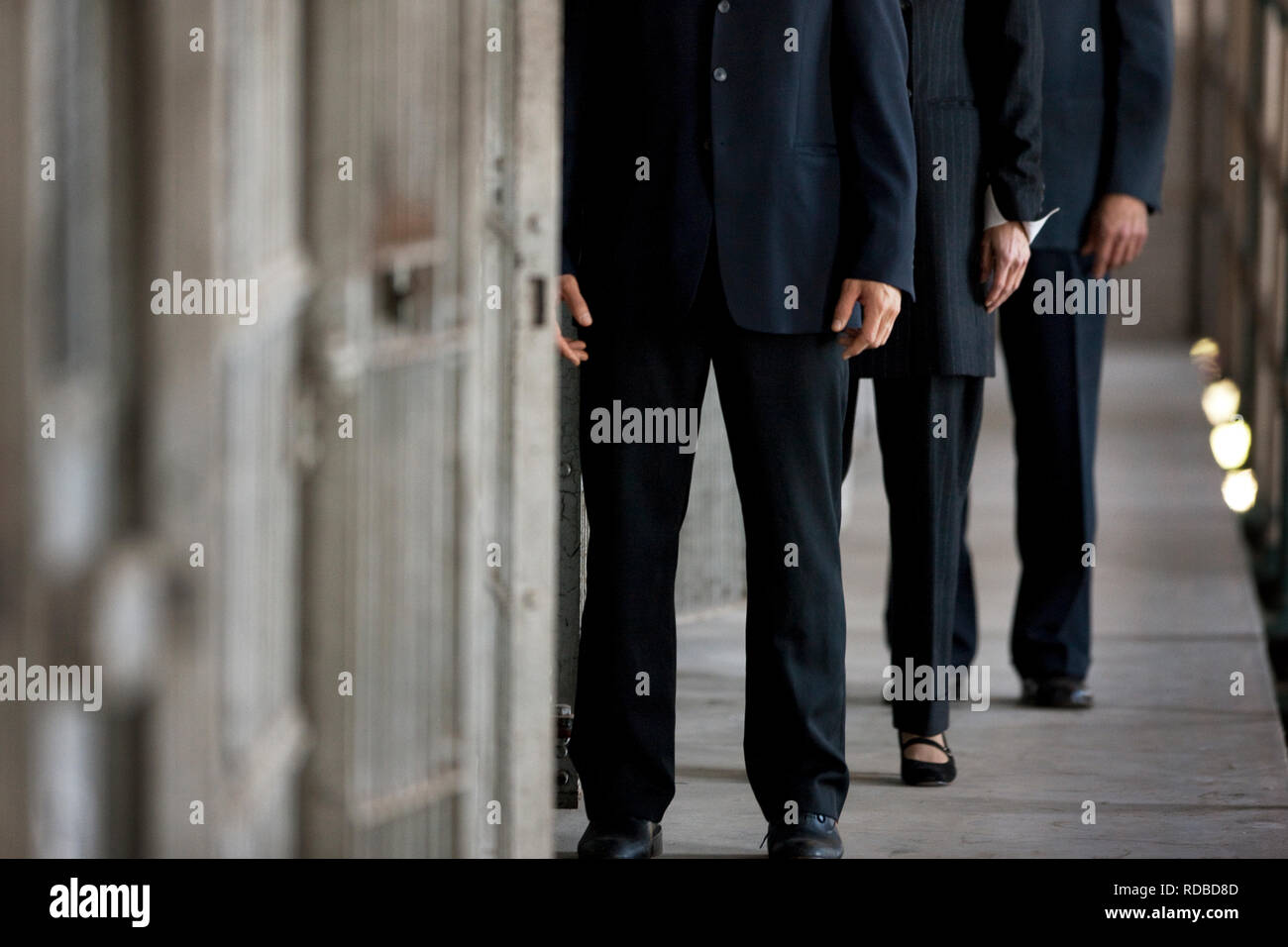 Three suited businesspeople standing next to a jail cell. Stock Photo