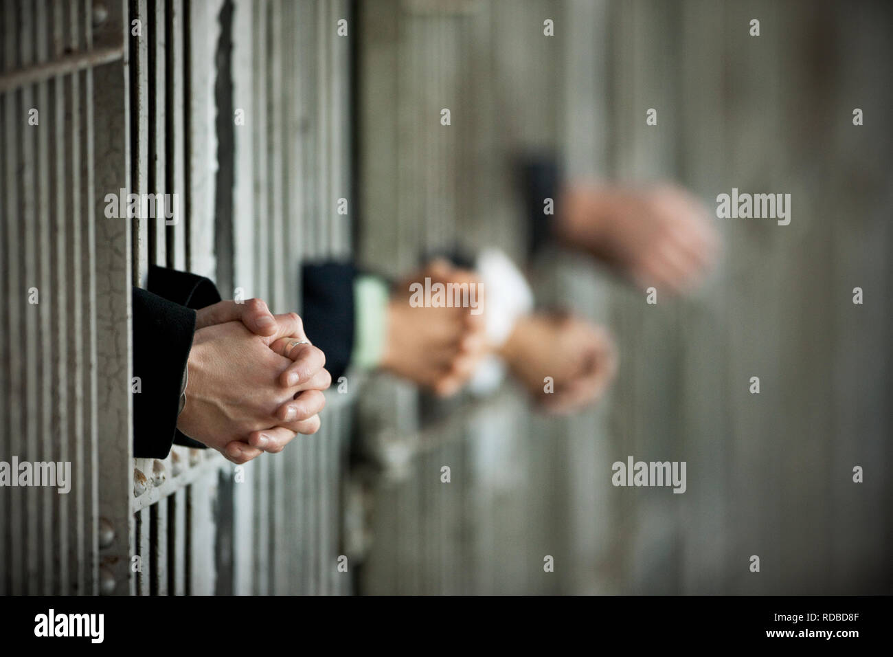 Hands of four businesspeople handing clasped in between the bars of a jail cell. Stock Photo
