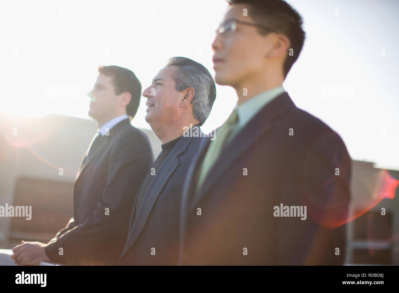 Three focused businessmen standing side by side outside in the sun. Stock Photo
