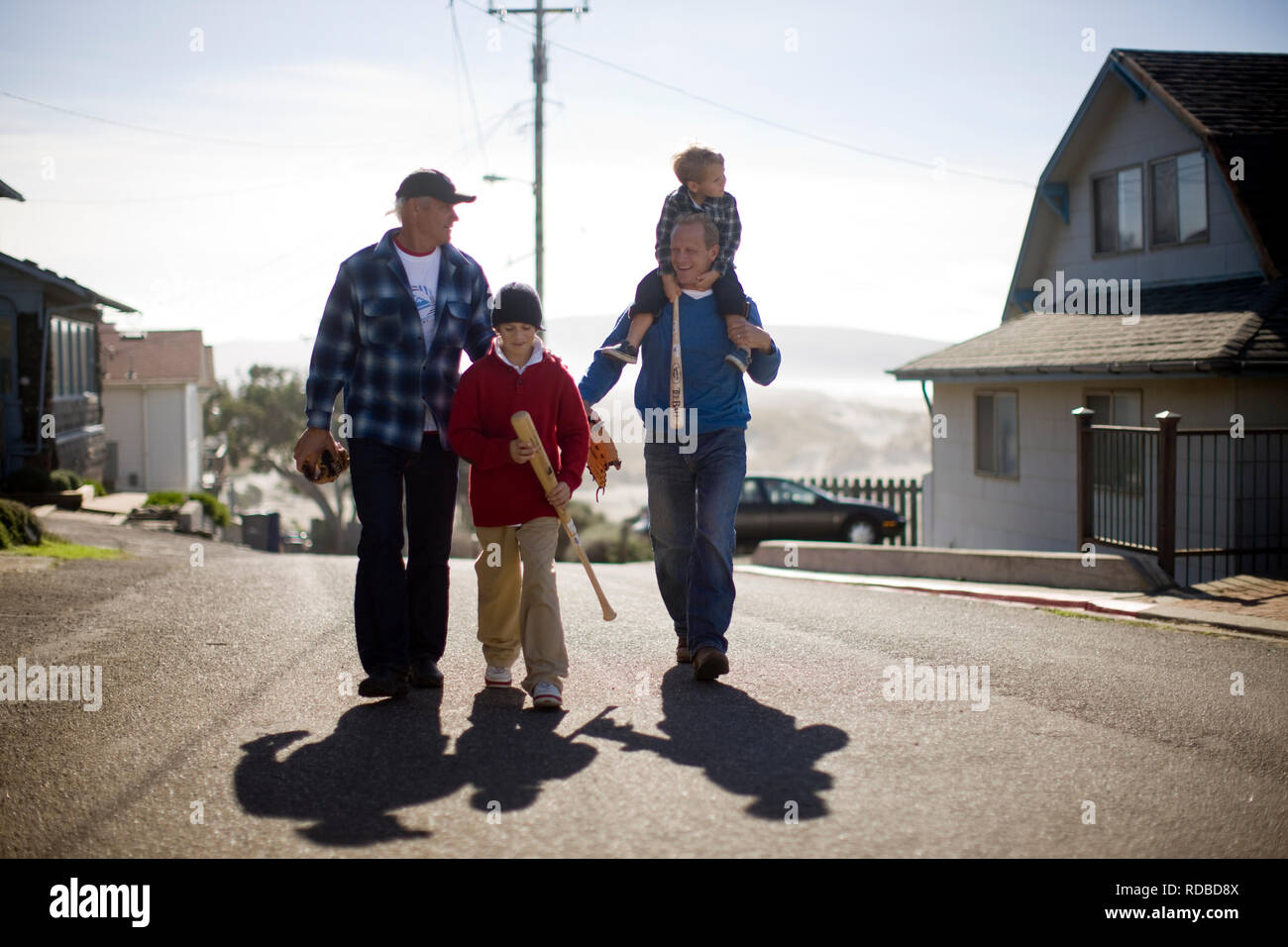 Two young boys walking with their fathers and holding softball gear Stock Photo