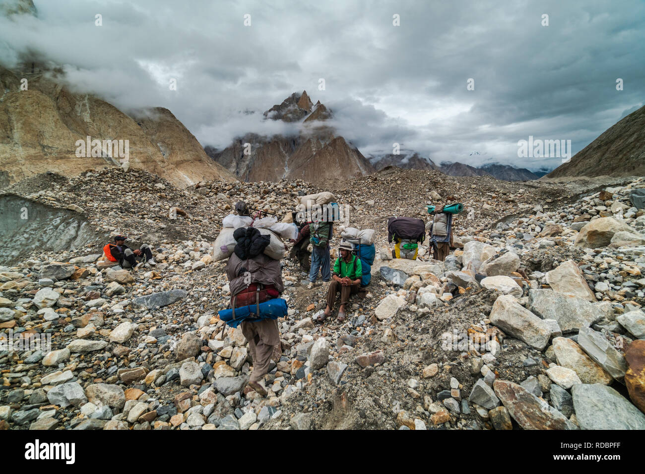 Karakoram, Pakistan - July 24, 2018: Sherpas with heavy loads having rest in Karakoram Mountain Range in Pakistan. Illustrative editorial. Stock Photo