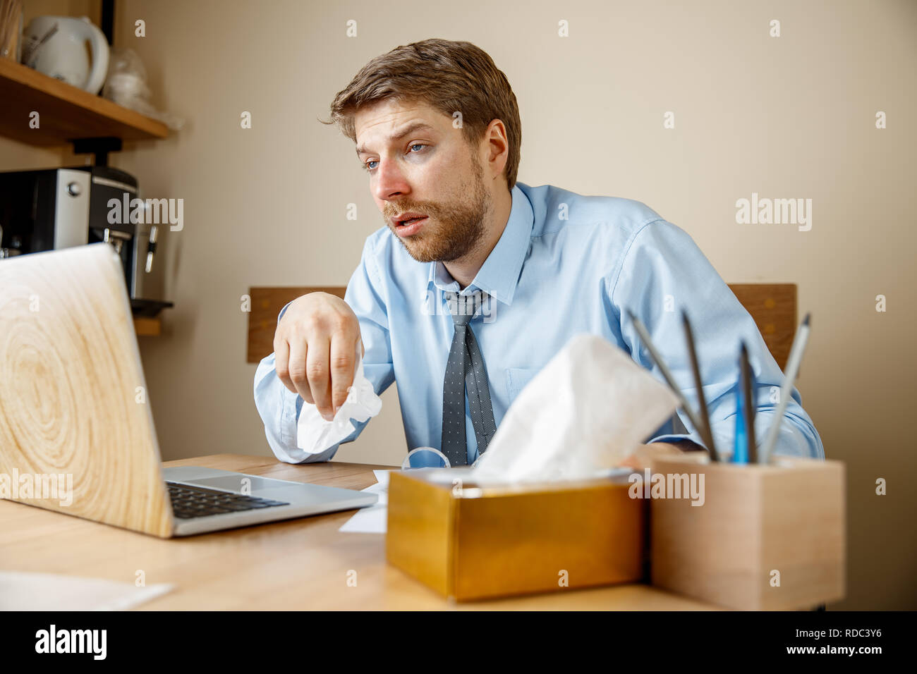 Sick man with handkerchief sneezing blowing nose while working in