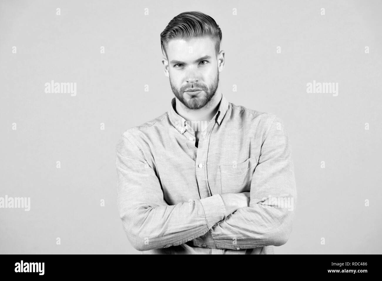 Bearded man keep arms crossed on grey background. Macho in blue tshirt with serious face. Tired after everyday work. Office dress code. Casual in style. Confidence and charisma. Young and handsome. Stock Photo