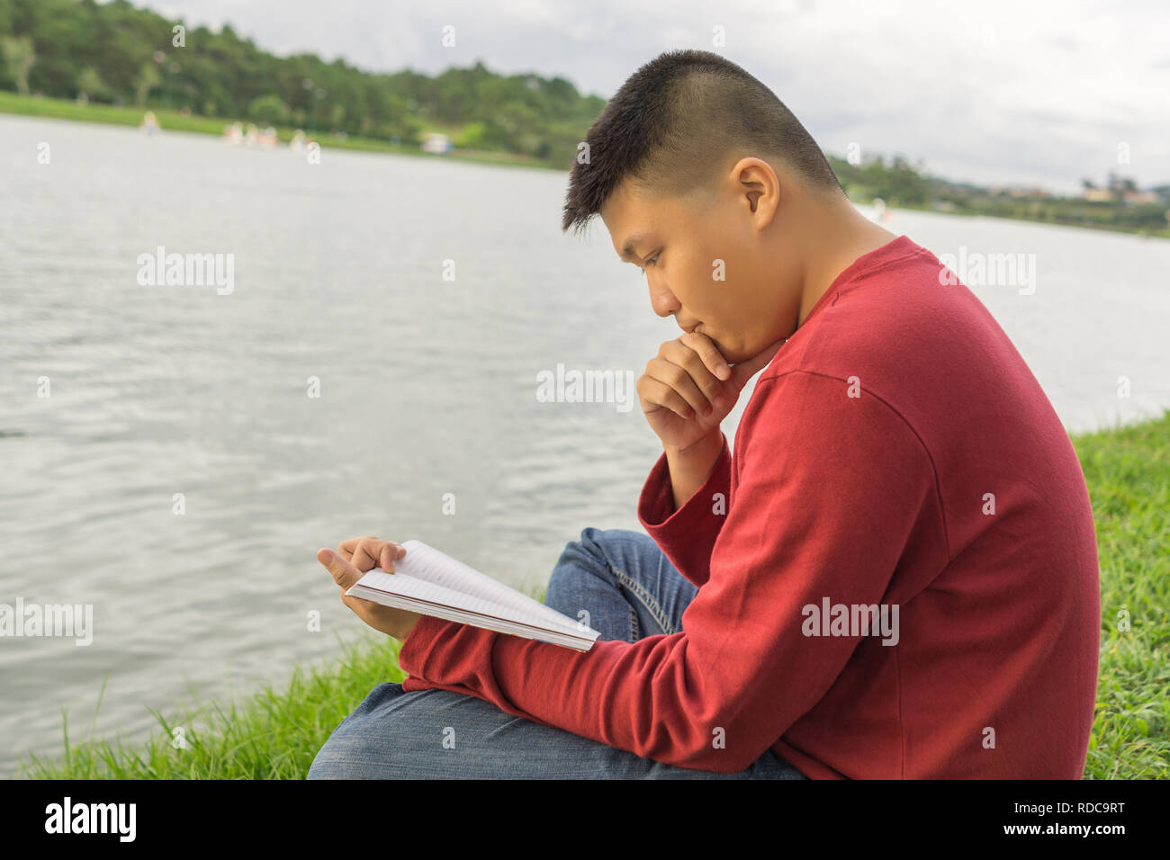 Asian man sitting on grass, reading book Stock Photo