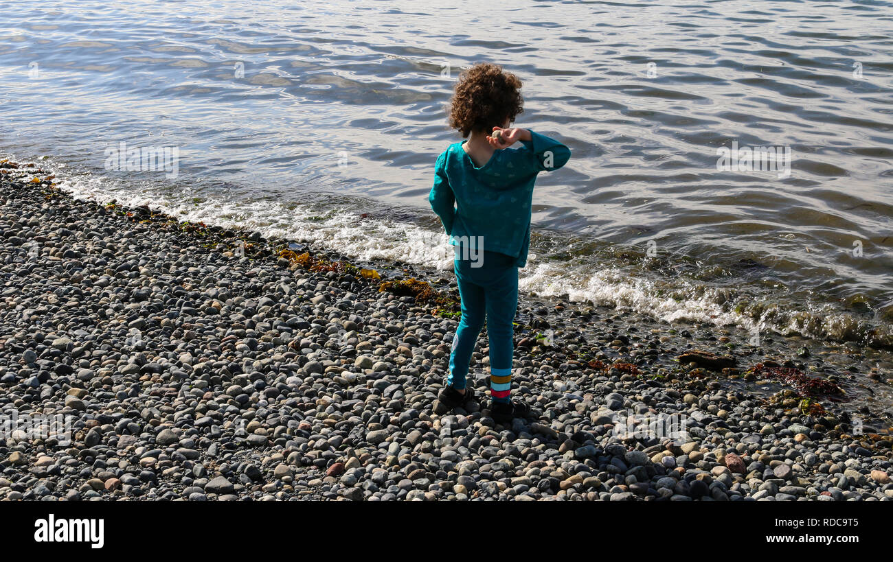 Young girl throwing rock into Pugeot Sound at Alki Beach in West Seattle, WA Stock Photo