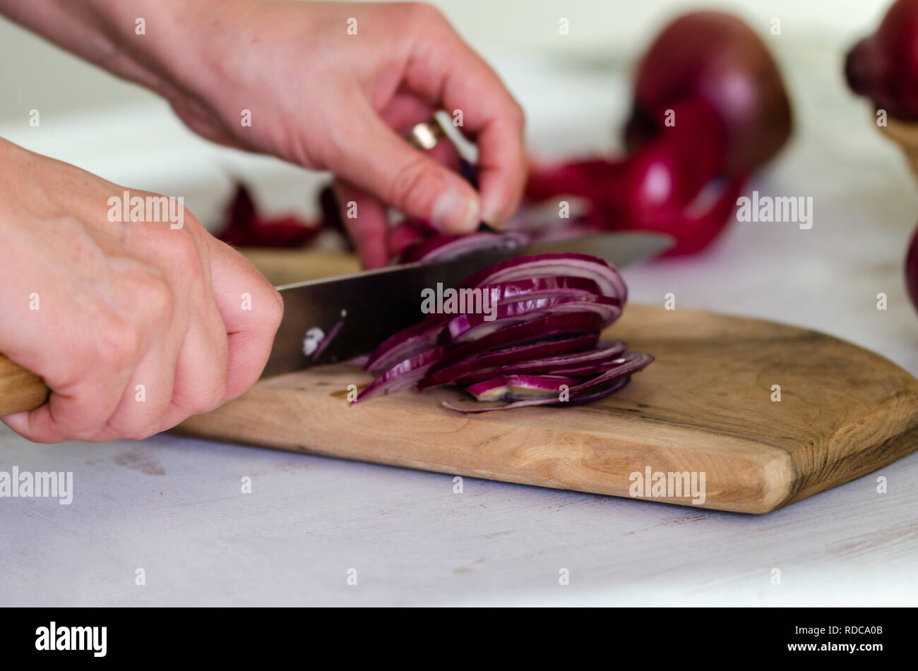 Woman is cuting red onion on wooden board Stock Photo - Alamy