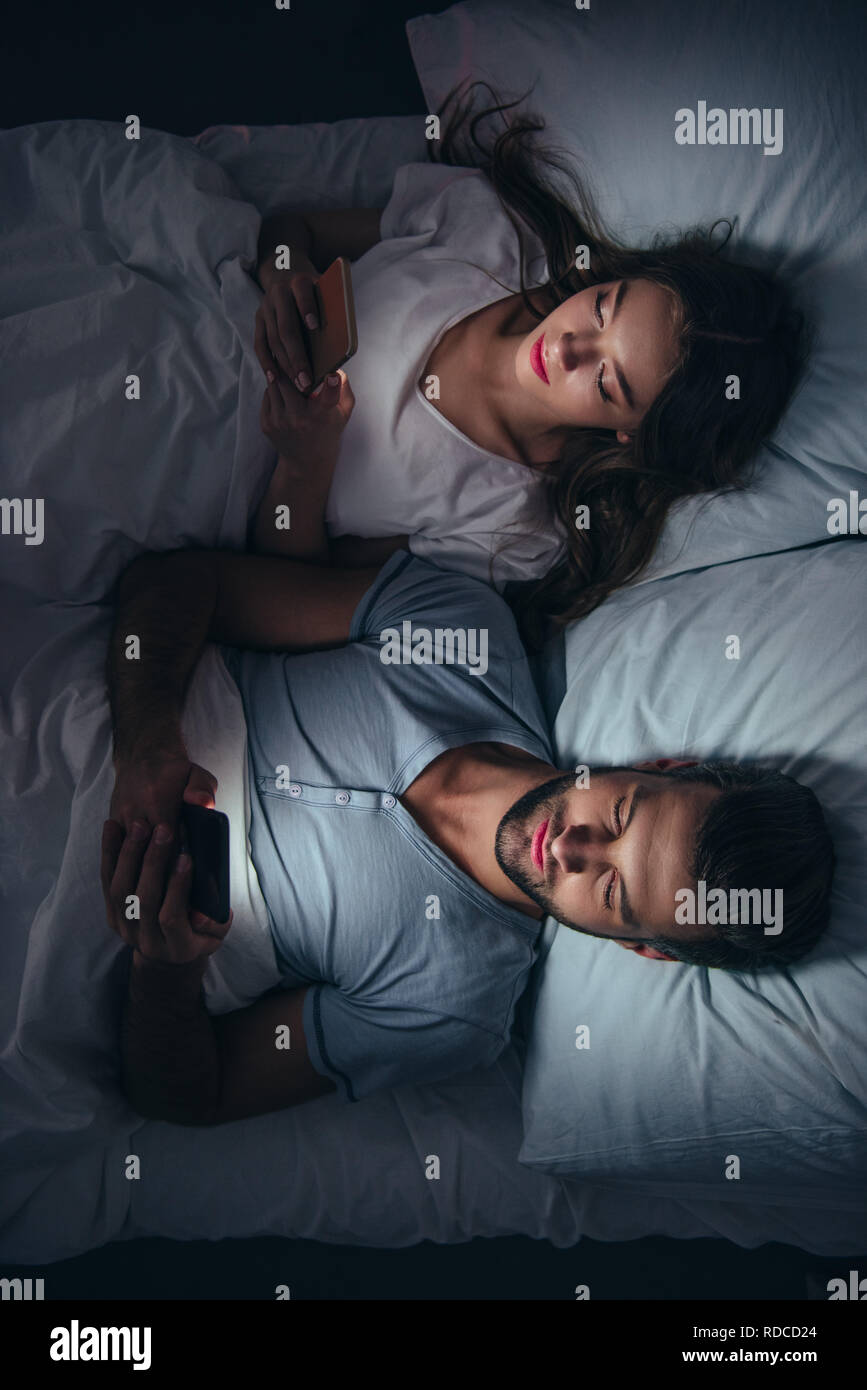 young couple lying in bed and using smartphones at night Stock Photo