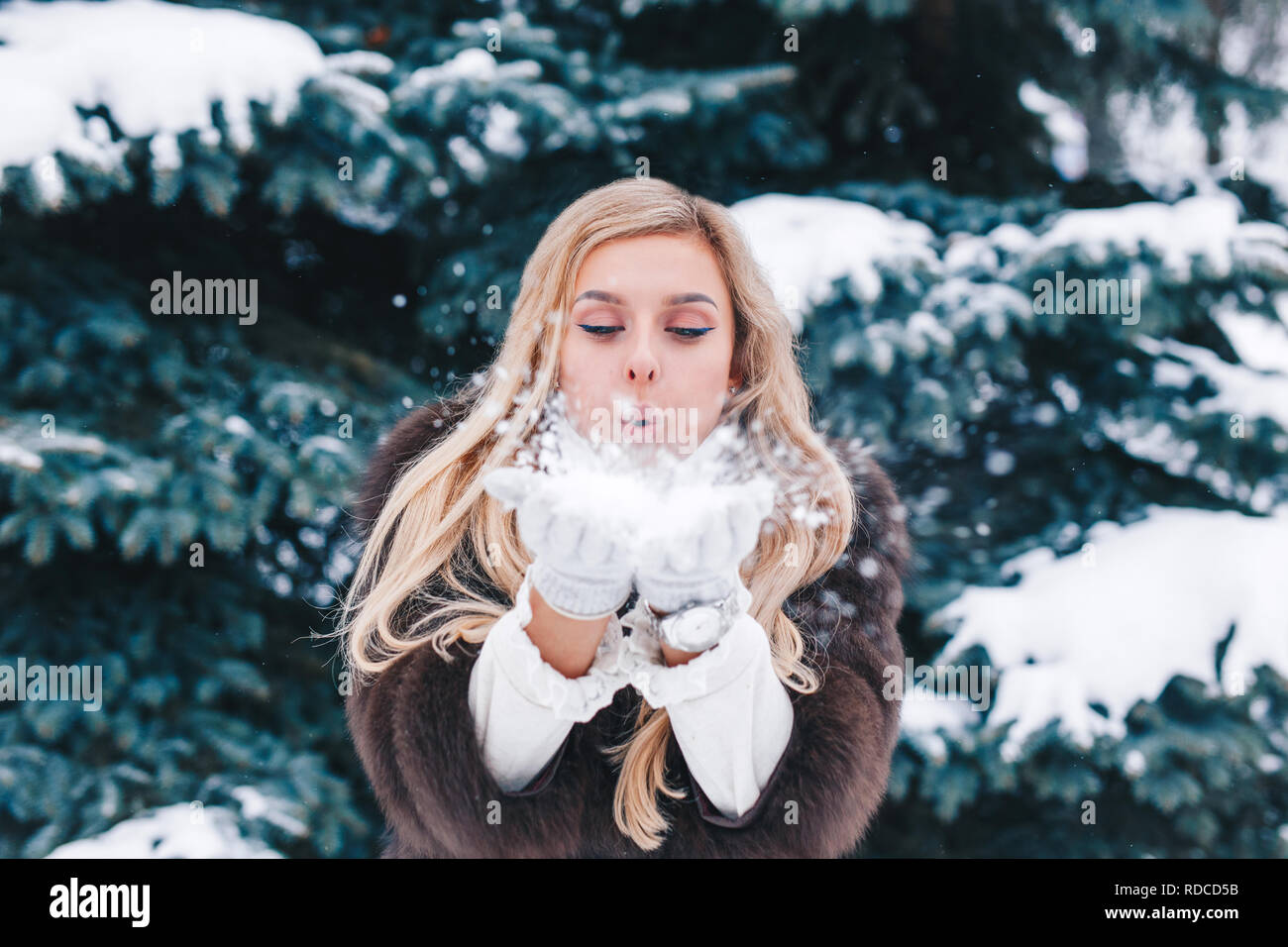 Beautiful girl in fashionable winter clothes blows snow from the