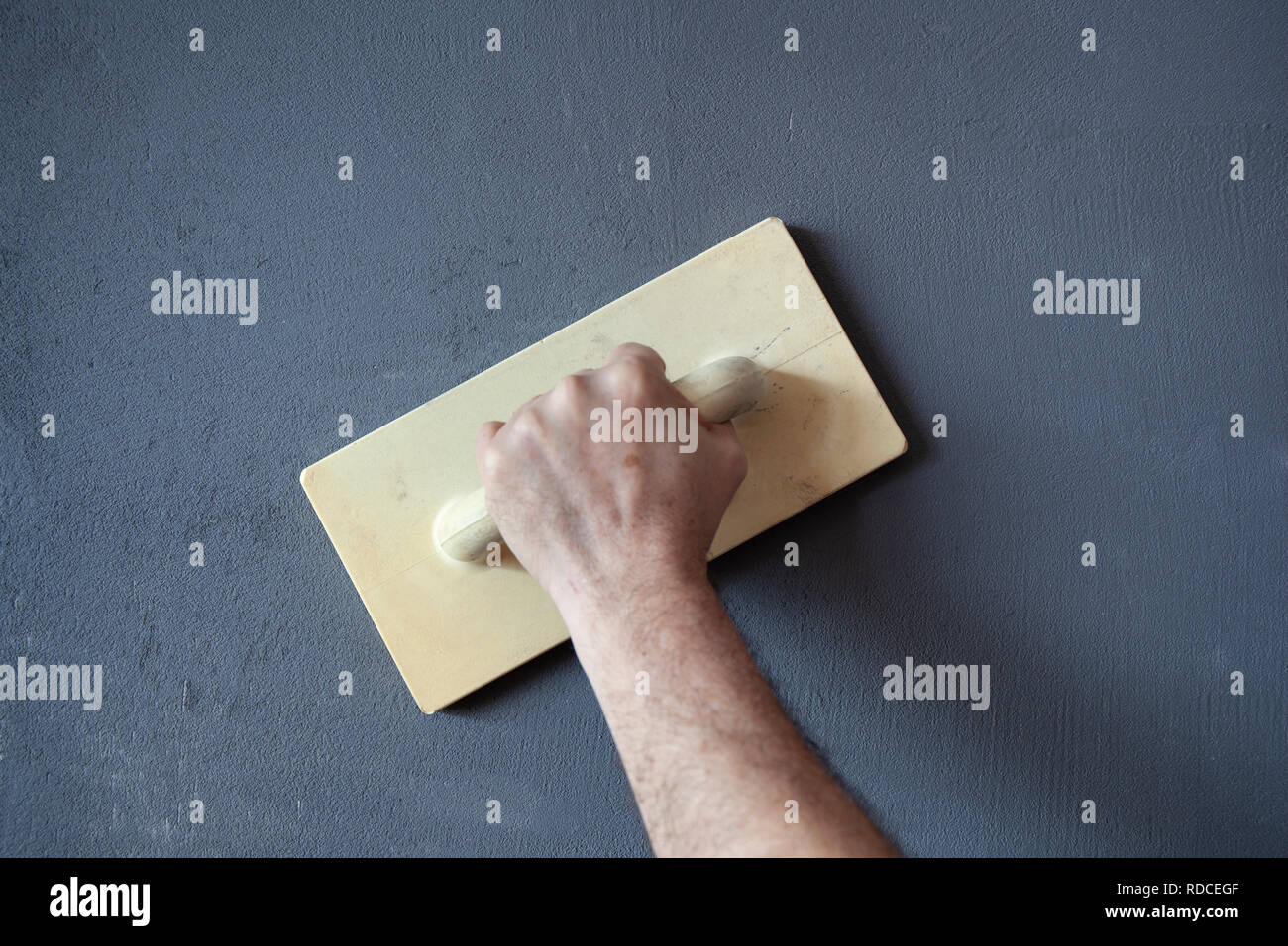 Hand with plastic trowel plastering and smoothing a wet concrete plastered wall. Stock Photo