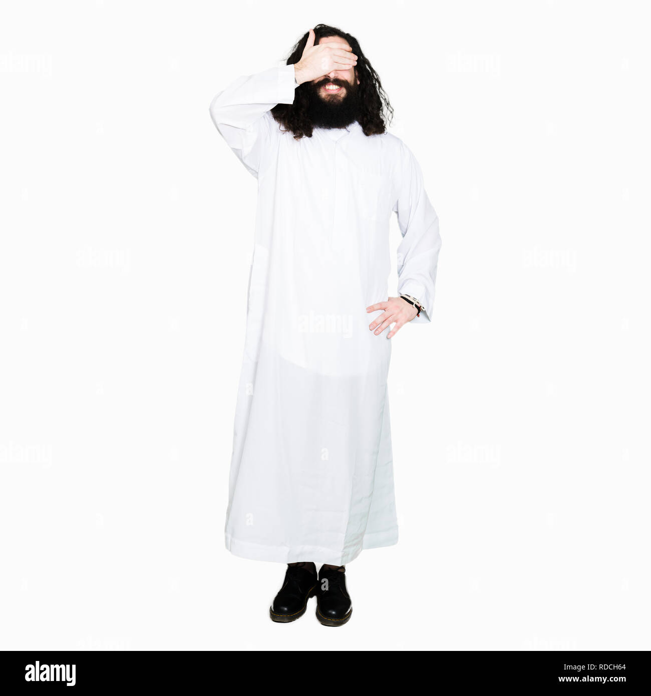 Man wearing Jesus Christ costume smiling and laughing with hand on face covering eyes for surprise. Blind concept. Stock Photo