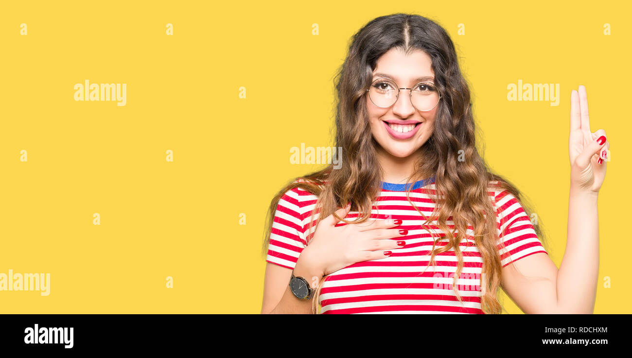 Young beautiful woman wearing glasses Swearing with hand on chest and fingers, making a loyalty promise oath Stock Photo