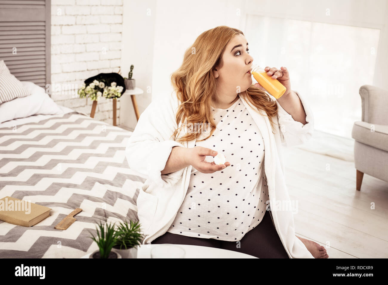 Big overweight young woman drinking freshly-made orange juice Stock Photo