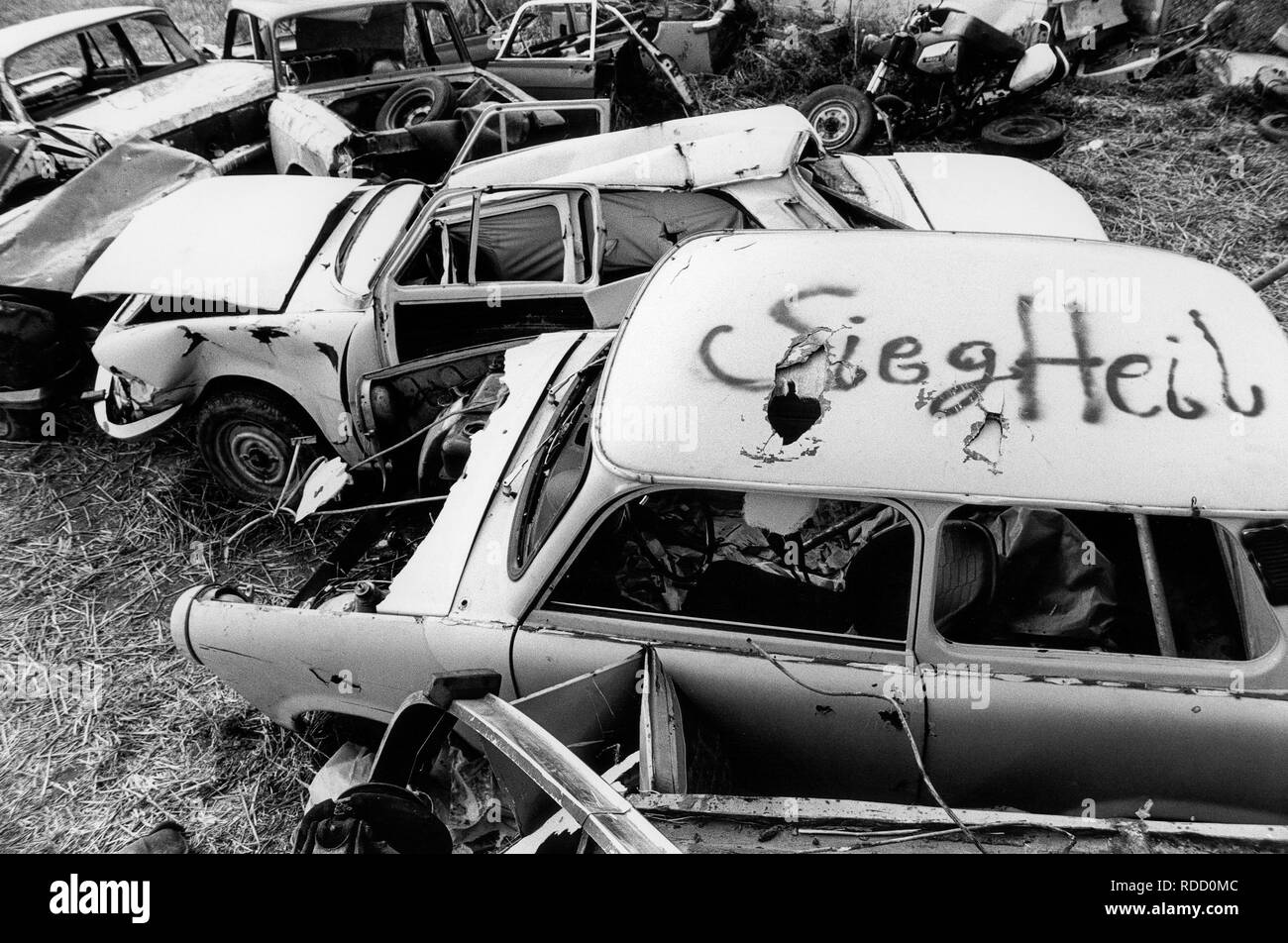 GERMANY in 1990 after reunification, former East Germany, German Democratic Republic GDR, typical plastic car Trabant also called Trabbi with fascist Nazi Hitler greeting Sieg Heil and Wartburg car on wild dumping site in village Plauerhagen, Mecklenburg, people have dumped their East German car in exchange to new western cars, scan from black and white negative with film grain Stock Photo
