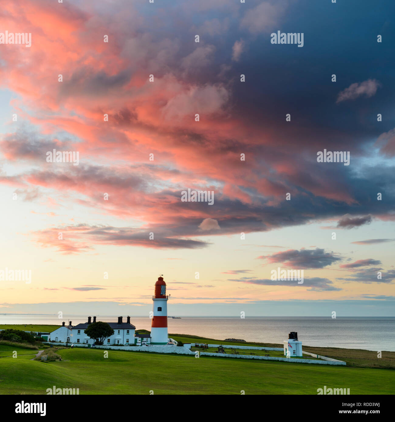 Huge colourful dramatic clouds are lit up by the sunset over Souter Lighthouse on the North East coast. Stock Photo