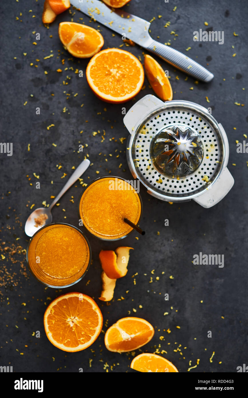 Summer drink. Fresh orange juice in tall glass with citrus squeezer and orange slices on dark concrete background. Top view, copy space for text. Sele Stock Photo