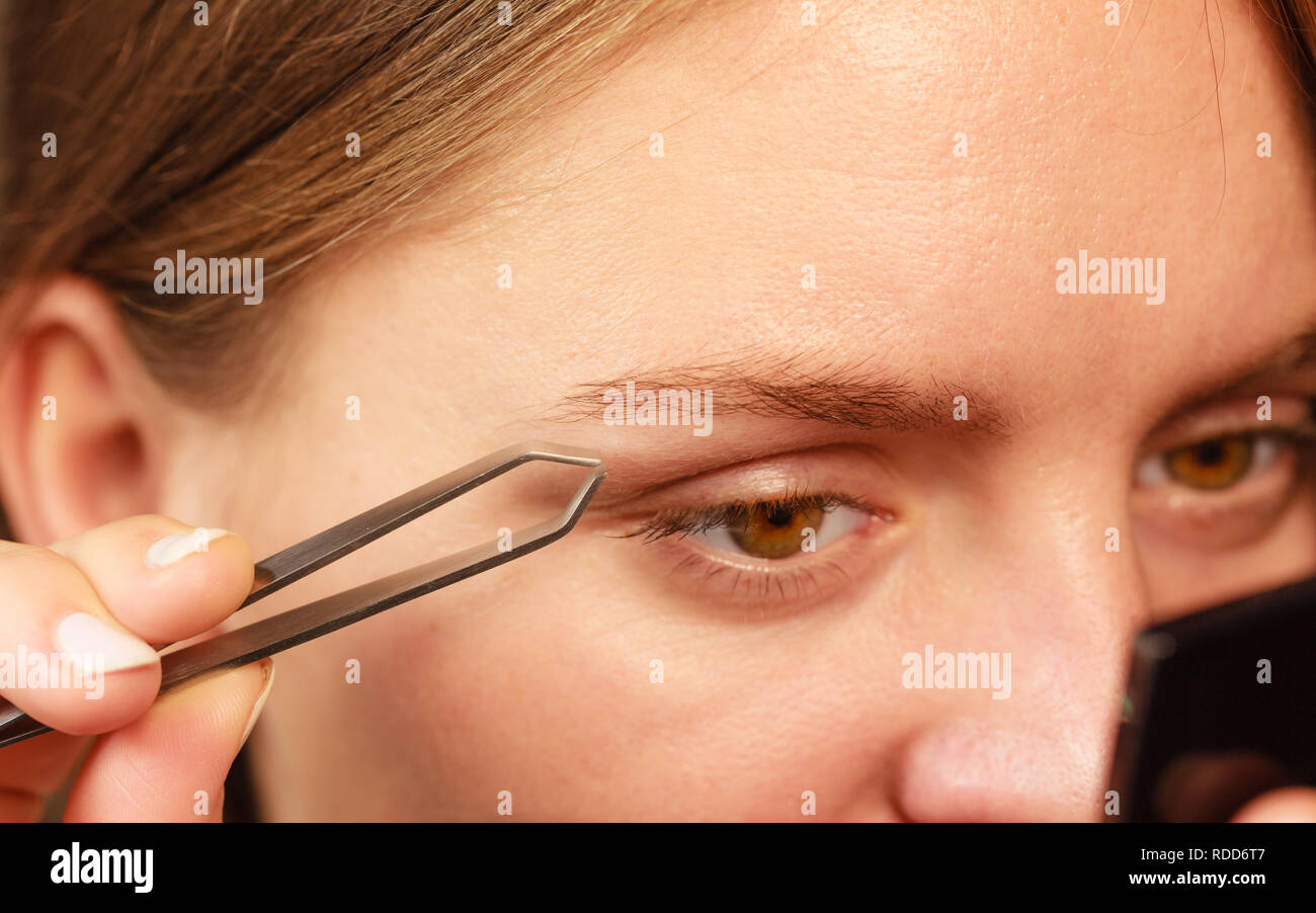 Woman plucking eyebrows depilating with tweezers closeup part of face