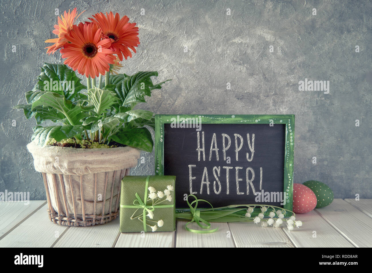 Spring flowers, Easter decorations and a blackboard on white table. Text 'Happy Easter!' on a blackboard. Stock Photo